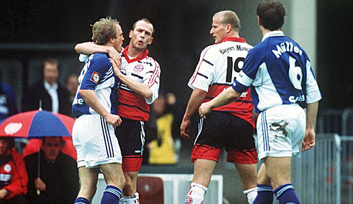 1998/99, München siegt 3:1 auf Schalke: Emotionen pur bei Mario Basler und Mike Büskens. Ottmar Hitzfeld schaut interessiert unterm Schirm zu