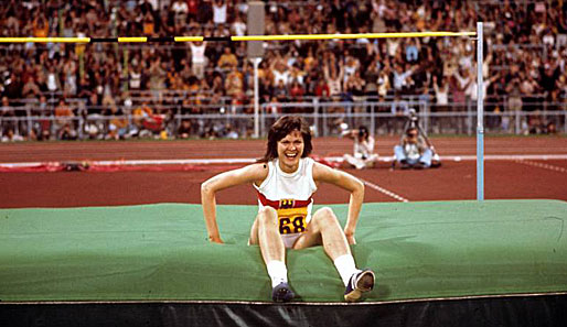 Ulrike Meyfarth sitzt lachend auf der Matte - kein Wunder, denn die Athletin hat grade Hochsprung-Gold geholt