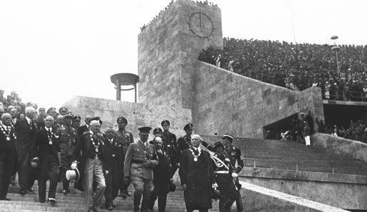Adolf Hitlers Propaganda-Maschinerie läuft. Der Führer betritt mit einem Tross von Funktionären und Staatsmännern das Stadion