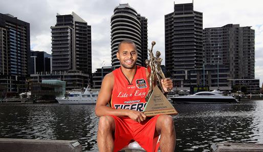 Basketball-Profi Patty Mills von den Melbourne Tigers posiert stolz mit dem NBL-Pokal am Central Pier vor den Wolkenkratzern Melbournes