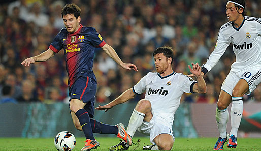 Xabi Alonso (m.), hier im Duell mit Lionel Messi (r.), sieht in Reals Spiel klare Unterschiede zu Barca