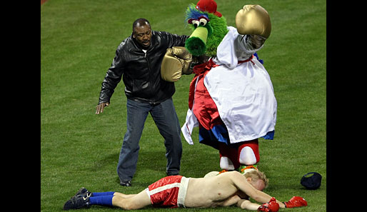 Spaß am Rande des 4. Spiels der World-Series: Phillies-Maskottchen Philly Fanatik knockt seinen Gegner aus. Schiedsrichter bei diesem Spektakel: Ex-Box-Weltmeister Joe Frazier