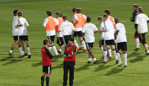 Auf geht's! Die Spieler laufen sich warm, während Jogi Löw und Co-Trainer Hansi Flick noch einmal die Trainingseinheit durchsprechen