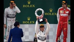 Während Hamilton sich über den Siegerpokal freuen darf, fällt Rosberg und Vettel ein Lächeln eher schwer...