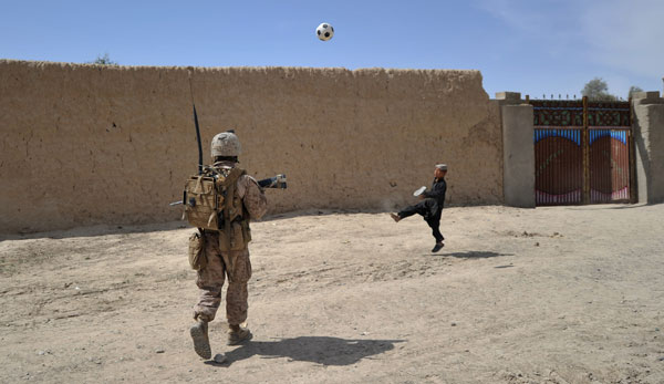 Ein afghanischer Junge spielt Fußball, während ein US-Marine patroulliert