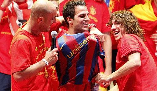 Sommer 2010: Nach Spaniens WM-Titel stecken Reina (l.) und Puyol (r.) Fabregas in ein Barca-Trikot