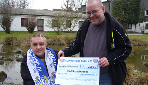 Ein Vertreter des Supporters Club e.V. übergibt Carl Ramsbottom (l.) den Spendenscheck
